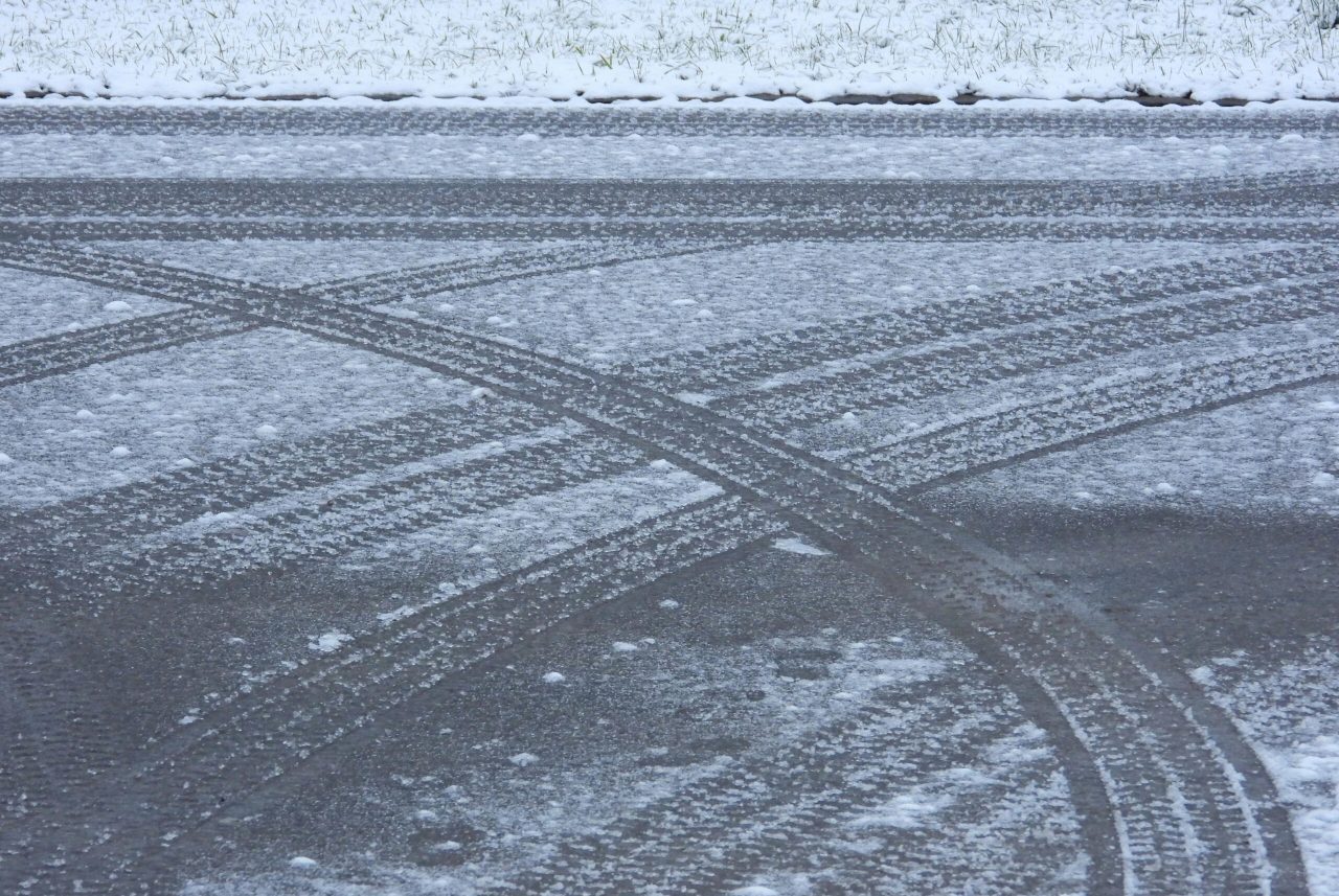 Snow-covered road with intersecting tire tracks and a dusting of snow, illustrating winter conditions.